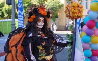 Woman in sugar skull facepaint and butterfly theme wings and outfit.